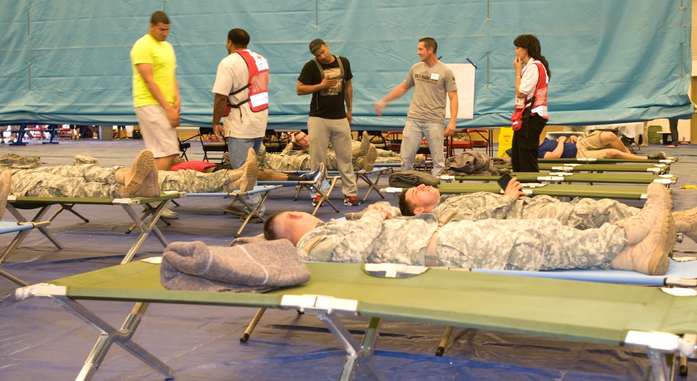 Red Cross volunteers help role-players among rows of cots during a disaster shelter training exercise.