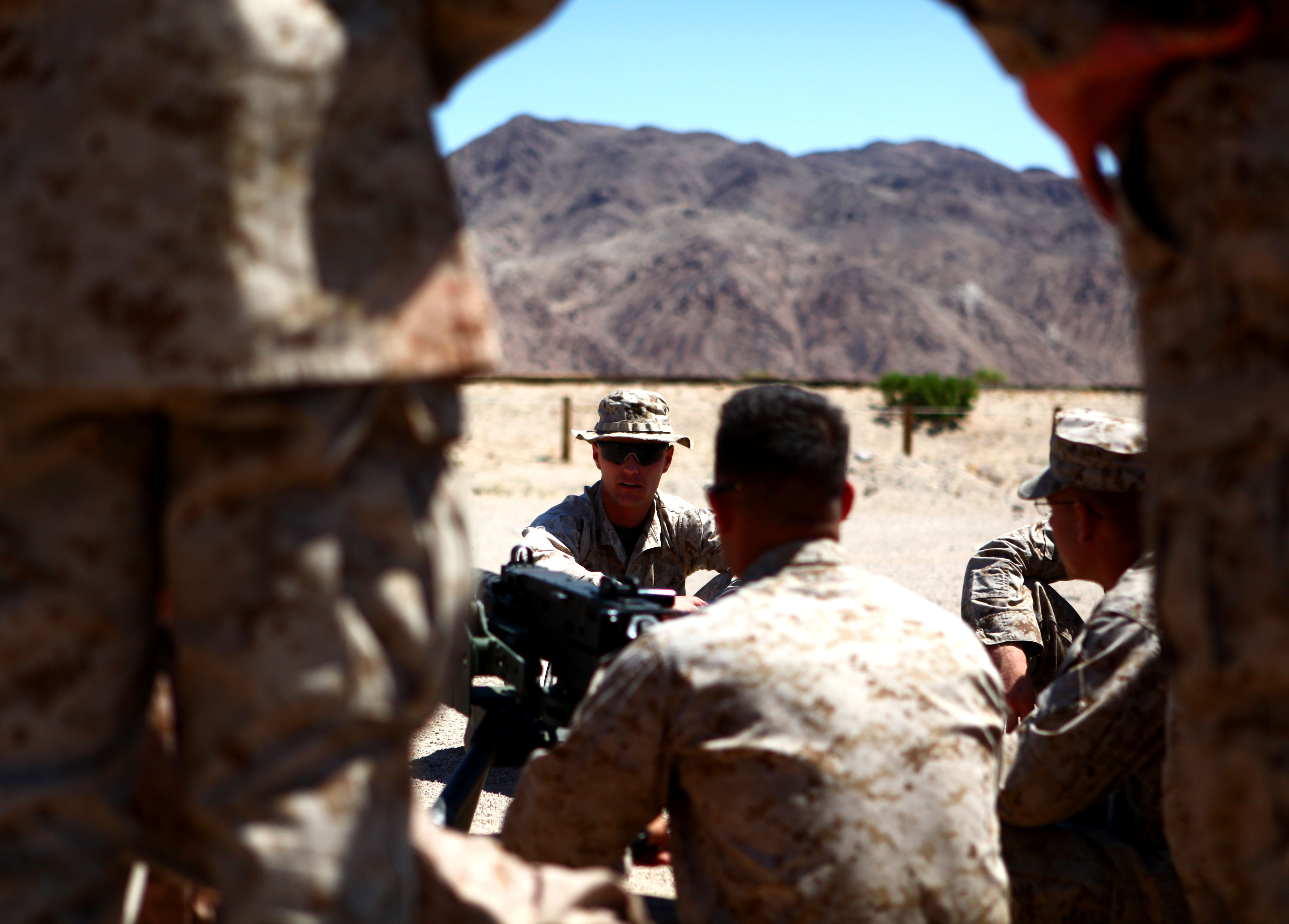 A Marine sergeant kneels behind a machine gun and briefs his Marines before a range in the Mojave Desert